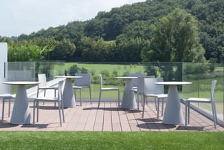 Moderne terrastafel met witte conische poot en grijze stoelen op houten terras, uitzicht op groen landschap en bosrand.