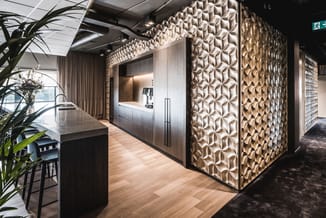Moderne kantoorruimte met beige 3D-wandpanelen, donker houten balie, zwart eiland, houten vloer en raampartij.