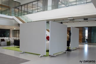 Modulaire witte scheidingswanden op wieltjes met groen gaas in modern kantoorinterieur met trap en glazen railing.