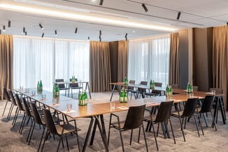 Moderne vergaderzaal met rechthoekige houten tafel, zwarte stoelen, groene flessen, grote ramen met gouden en witte gordijnen