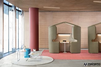 Moderne kantoorruimte met groene akoestische belcellen, roze kolom, houten wand, ronde tafel met blauwe elementen en rood tap