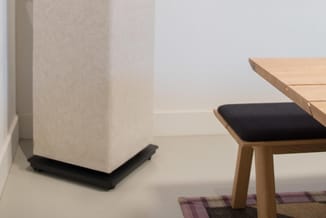 Houten bureau met zwart zitkussen naast beige akoestische paneel met zwarte voet in minimalistisch interieur.