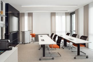 Moderne vergaderkamer met twee witte rechthoekige vergadertafels met zwarte onderstel, zwarte en oranje kantoorstoel, wandmon