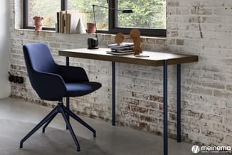 Moderne werkplek met donkerblauwe draaistoel, houten bureau met wit blad, zwarte metalen poten, zwarte bureaulamp en accessoi