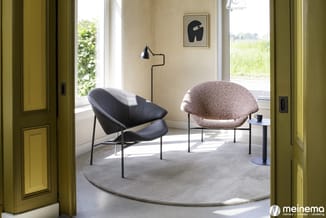 Twee modern design stoelen in een lichte ruimte: een zwarte leren stoel en een grijsbruine stoel met ronde zitting, op grijs