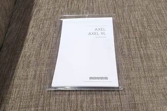 Handleiding voor Axel en Axel XL stoelen van Gis Papavoine, in doorzichtige verpakking op grijze stofsofa.