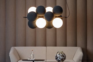 Moderne hanglamp met acht bollen in zwart en wit, boven beige lounge bank met glazen tafel en decoratief object, tegen vertic