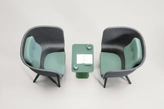 Twee grijze fauteuils met groen/grijs textiel en zwarte poten tegenover elkaar, met groen akoestisch scherm ertussen.