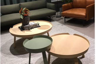 Moderne kantoorinrichting met grijze bank, cognackleurige fauteuil, ronde houten salontafels en groene bijzettafel op grijs t