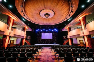 Bioscoop met zwarte stoelen in rijen, oranje plafond met draaiende structuur, blauwe spotlights, projectiescherm en rode gord