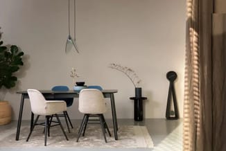 Moderne eetkamer met zwart bureau, twee witte stoelen, blauwe accessoires, zwarte decoratieve objecten, hangende lamp, plante