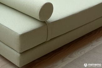 Beige linnen bank met cylindrische hoofdsteun, geplaatst op houten vloer in minimalistisch interieur.