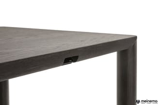 Grijshouten tafel met donker gebeitsde afwerking en zwart metalen kabelgoot onder het blad, detail van hoek en poot.