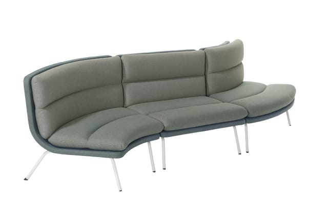 Grijze loungbank met gebogen vorm, gestoffeerd zitgedeelte, hoge rugkussens en witte aluminium poten.
