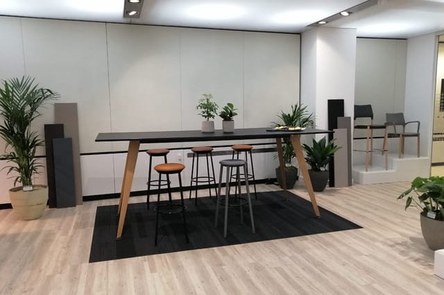Moderne kantoorruimte met zwarte houten vergadertafel op houten poten, barkrukken, zwart tapijt, potplanten en grijze wandpan