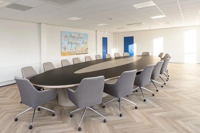 Moderne vergaderzaal met zwarte ovale vergadertafel, grijze kantoorstoelen met wieltjes en aluminium onderstel, witte plafond