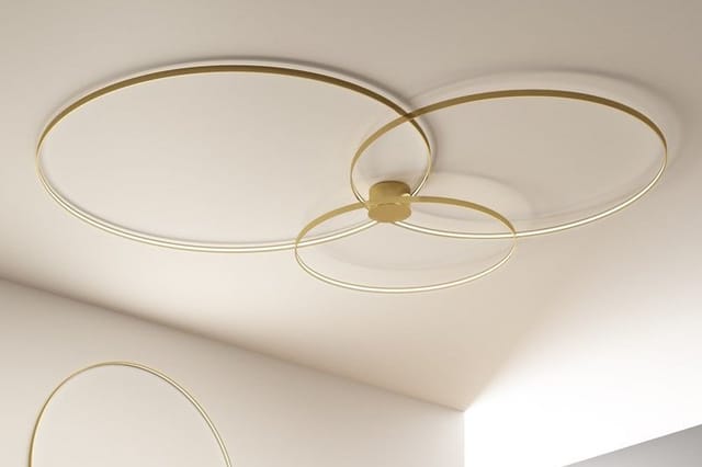 Goudkleurige plafondlamp met drie overlappende cirkelvormige ringen tegen wit plafond.