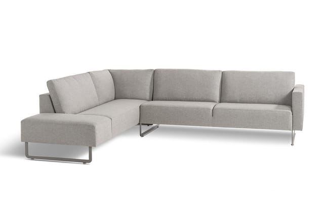 Grijze hoekbank met chaise longue links, metallic poten, modulair design op witte achtergrond.
