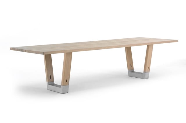 Lange houten vergadertafel met licht natuurkleurig blad en twee betonnen trapeziumvormige poten met houten kolommen.