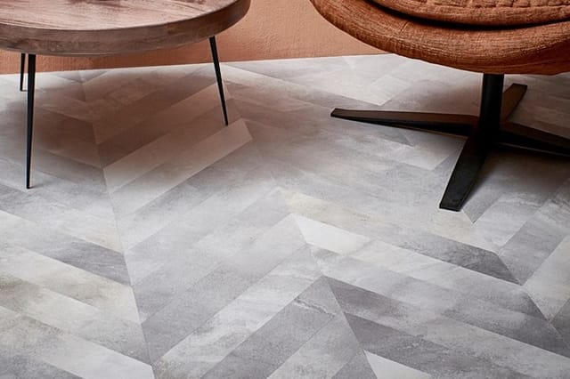 Twee ronde houten tafels met metalen poten op grijze geometrische vloer in visgraatpatroon.