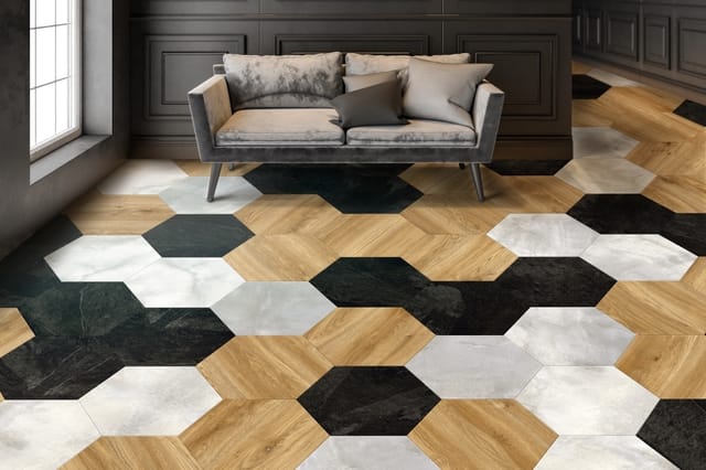 Grijze stof sofa met kussens in moderne woonkamer met hexagonale vloertegels in hout, wit en zwart.