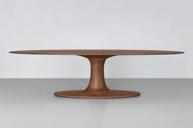 Houten vergadertafel met ovaal blad en centrale voetsteun, donkerbruin gelakt, op neutraal grijze ondergrond.