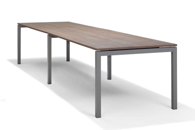 Lange vergadertafel met grijs metalen onderstel en grijsbruin houten blad, vier poten, veel zitcapaciteit.